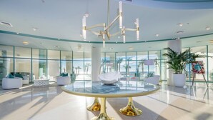 En modern entréhall med ett stort glasbord i mitten, vita soffor och en kristallkrona.
