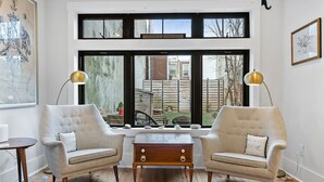Ein Zimmer mit zwei Sesseln, einem kleinen Holztisch und einem großen Fenster mit vielen Fensterscheiben.