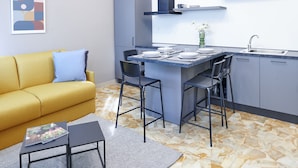 Un espacio habitable compacto con sofá, una pequeña mesa de comedor y una zona de cocina con mostrador tipo bar.