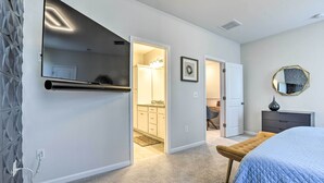 A bedroom with a large bed, a bench, a wall-mounted TV, and a bathroom visible through an open door. - Tasteful Durham Townhome - 6 Mi to Downtown! (Durham)