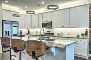 A modern kitchen with white cabinets, stainless steel appliances, a granite countertop, and three wooden bar stools. - Tasteful Durham Townhome - 6 Mi to Downtown! (Durham)