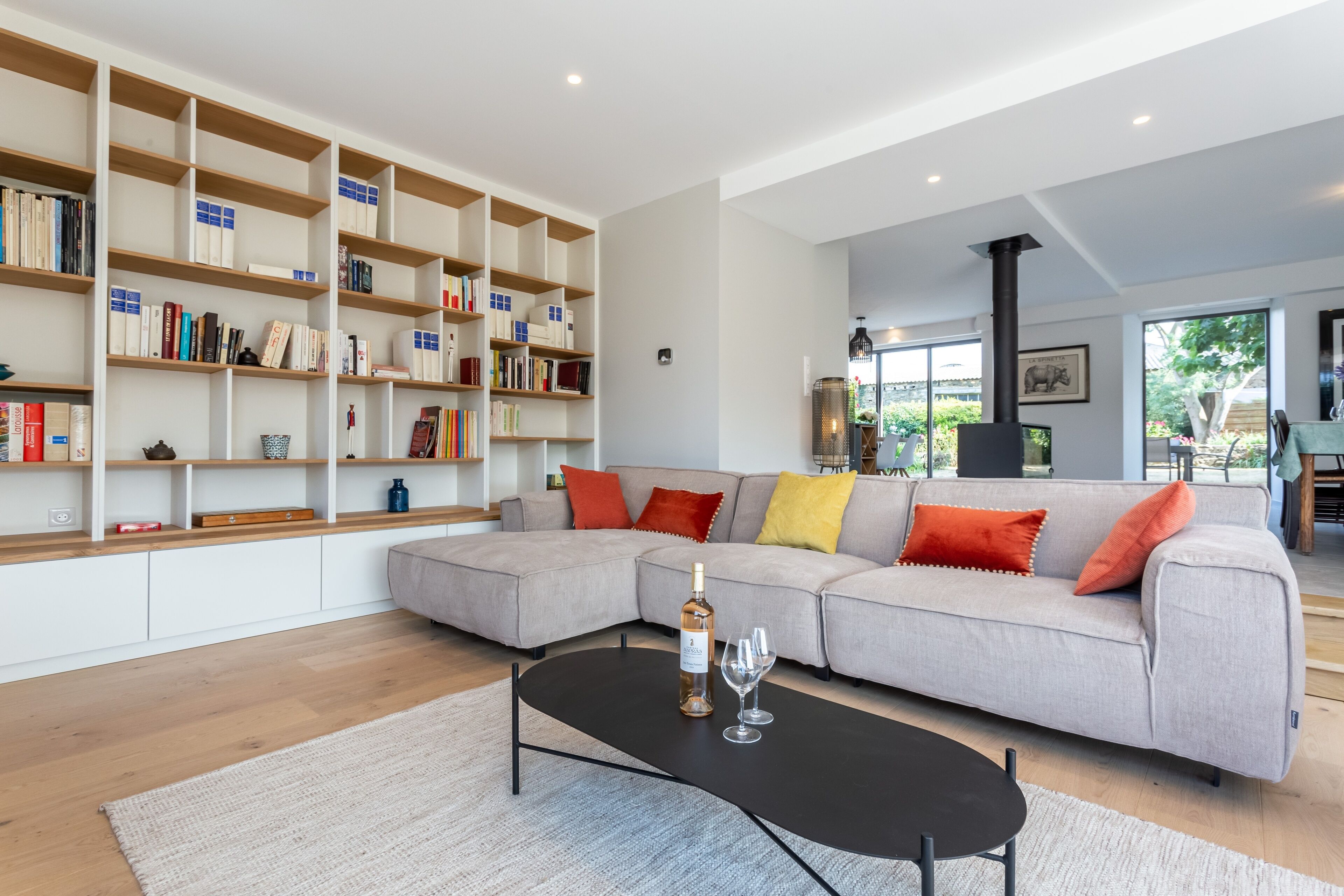 Una sala de estar moderna con un sofá modular, una mesa de centro negra y una estantería llena de libros y objetos decorativos.