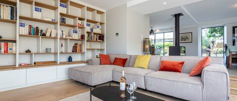Una sala de estar moderna con un sofá modular, una mesa de centro negra y una estantería llena de libros y objetos decorativos.