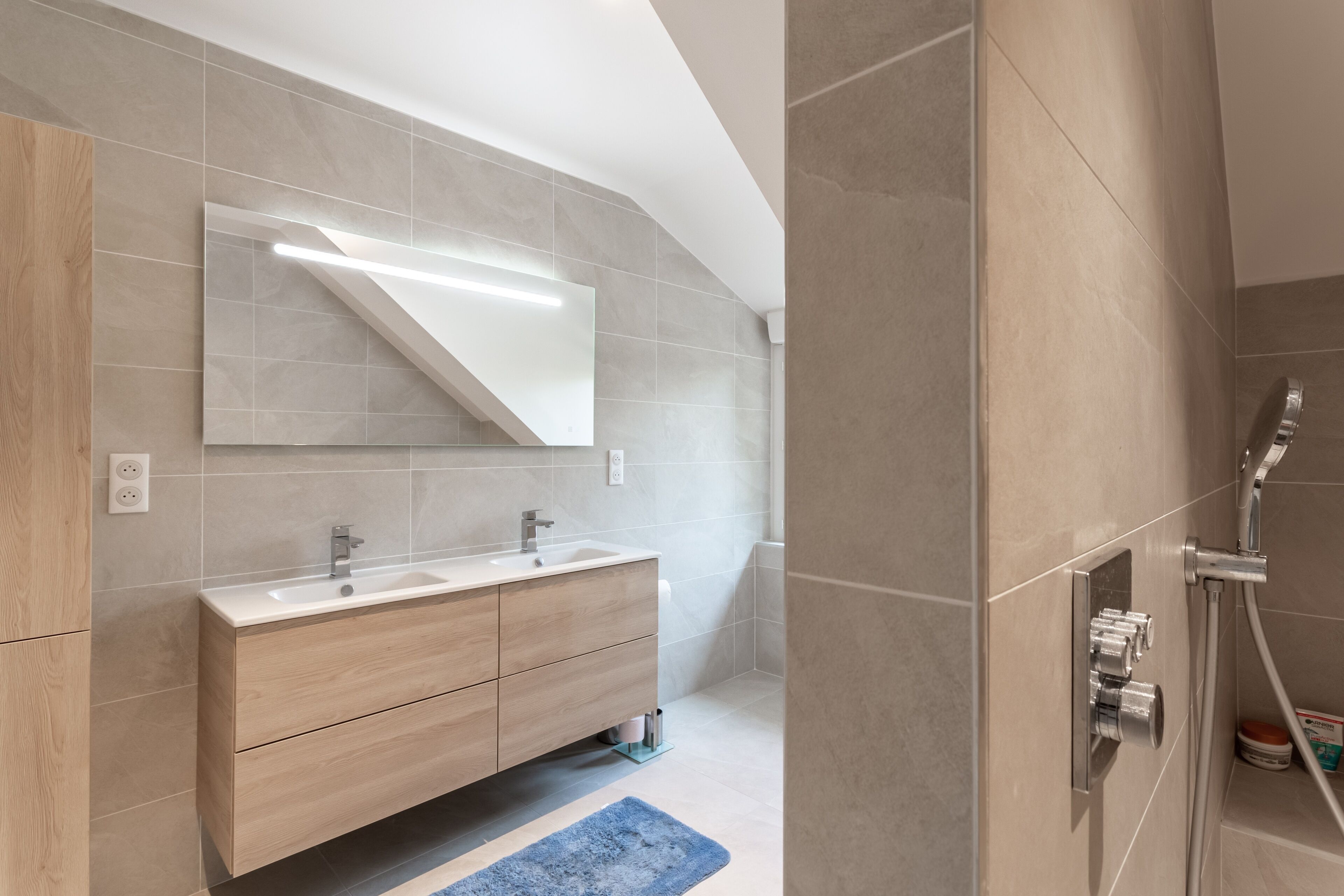 A modern bathroom with a wooden vanity, a large mirror, and a shower area.