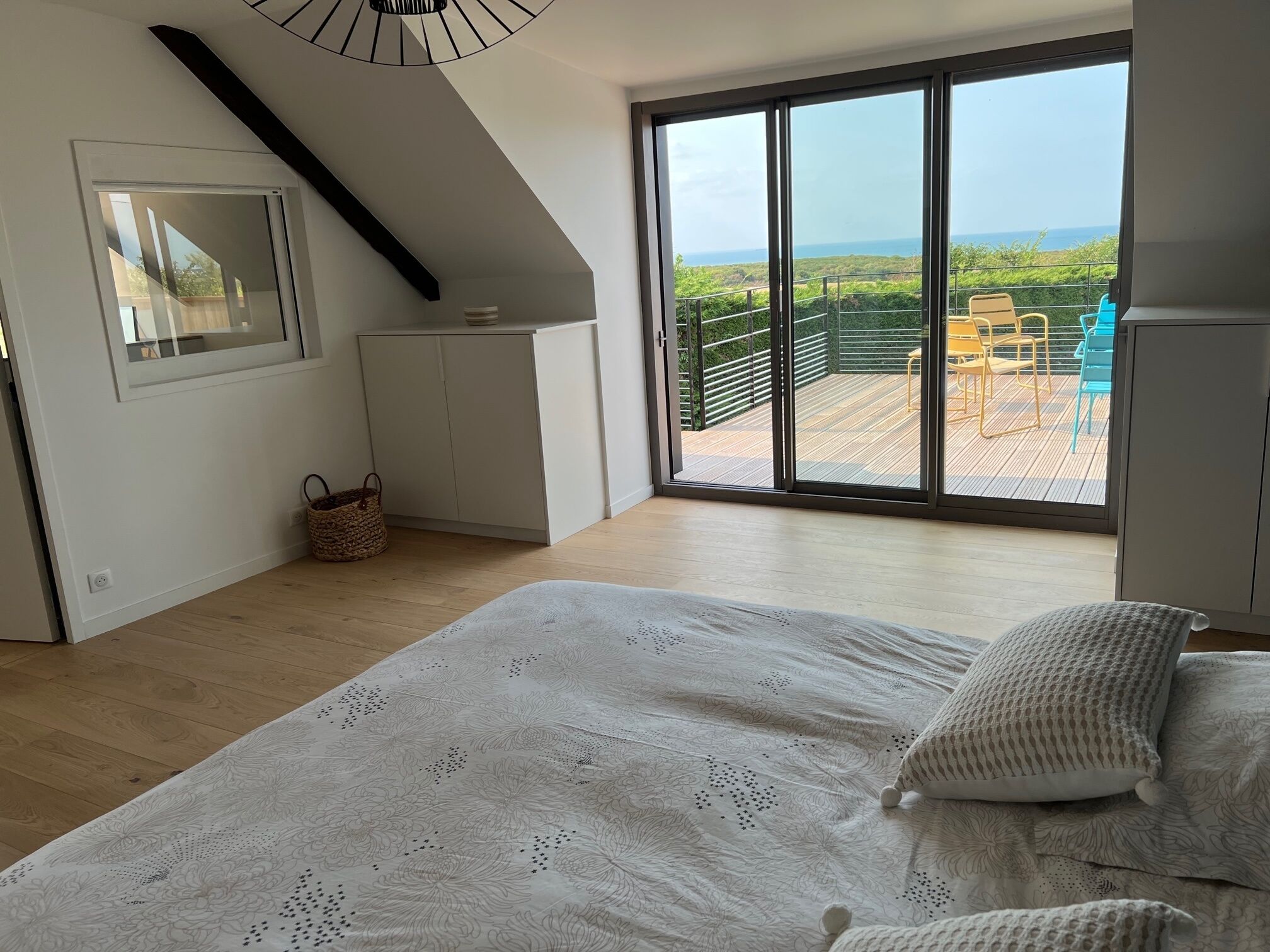A bedroom with a large bed, a view of a balcony with outdoor furniture, and a white wardrobe.