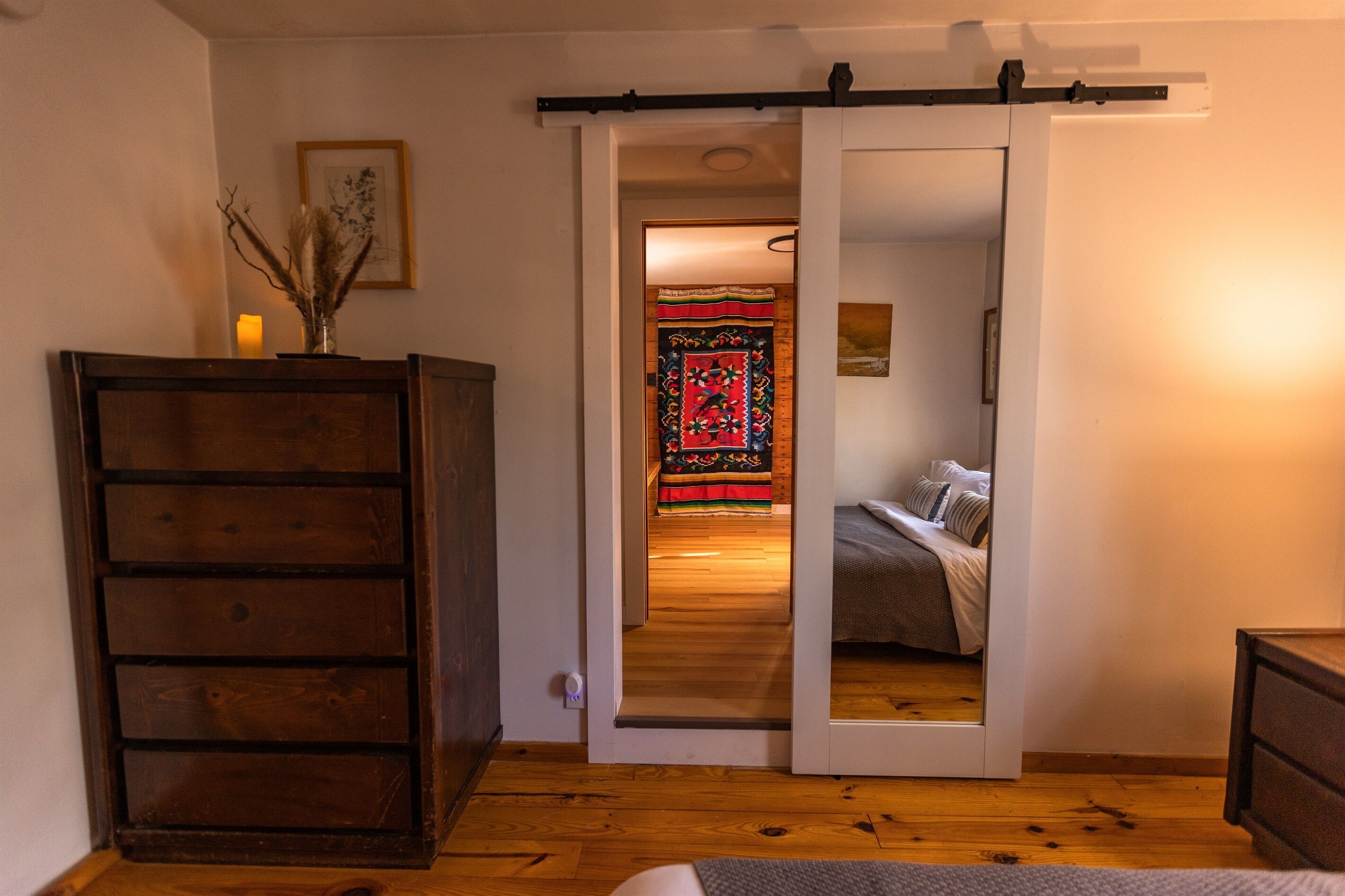 A bedroom with a wooden dresser, a bed with a striped bedspread, and a sliding door leading to another room.