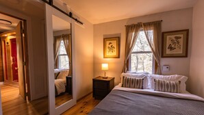 A bedroom with a large bed, a nightstand, a mirror, and two framed pictures on the wall. - Cozy Cottage Near Hiking, Infrared Sauna & Fireplace | Dream House in the Gunks (Kerhonkson)