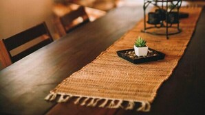 A dining area with a long wooden table, a woven placemat, and a small potted plant. - Cozy Cottage Near Hiking, Infrared Sauna & Fireplace | Dream House in the Gunks (Kerhonkson)