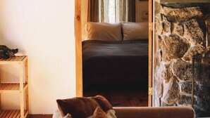 A cozy room with a bed, a stone fireplace, and a wooden ceiling. - Cozy Cottage Near Hiking, Infrared Sauna & Fireplace | Dream House in the Gunks (Kerhonkson)