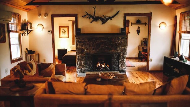 A cozy living room with a stone fireplace, a sofa, and a coffee table. - Cozy Cottage Near Hiking, Infrared Sauna & Fireplace | Dream House in the Gunks (Kerhonkson)