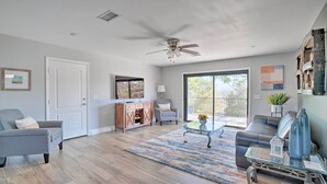 A spacious living room with hardwood flooring, a ceiling fan, a large window, and a sliding glass door leading to a balcony.