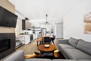 A modern living room with a fireplace, grey sofa, and a dining area with a wooden table and chairs.