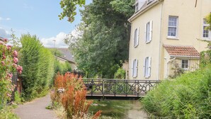 A narrow pathway leading to a building with a bridge over a water body, surrounded by greenery and a clear sky.