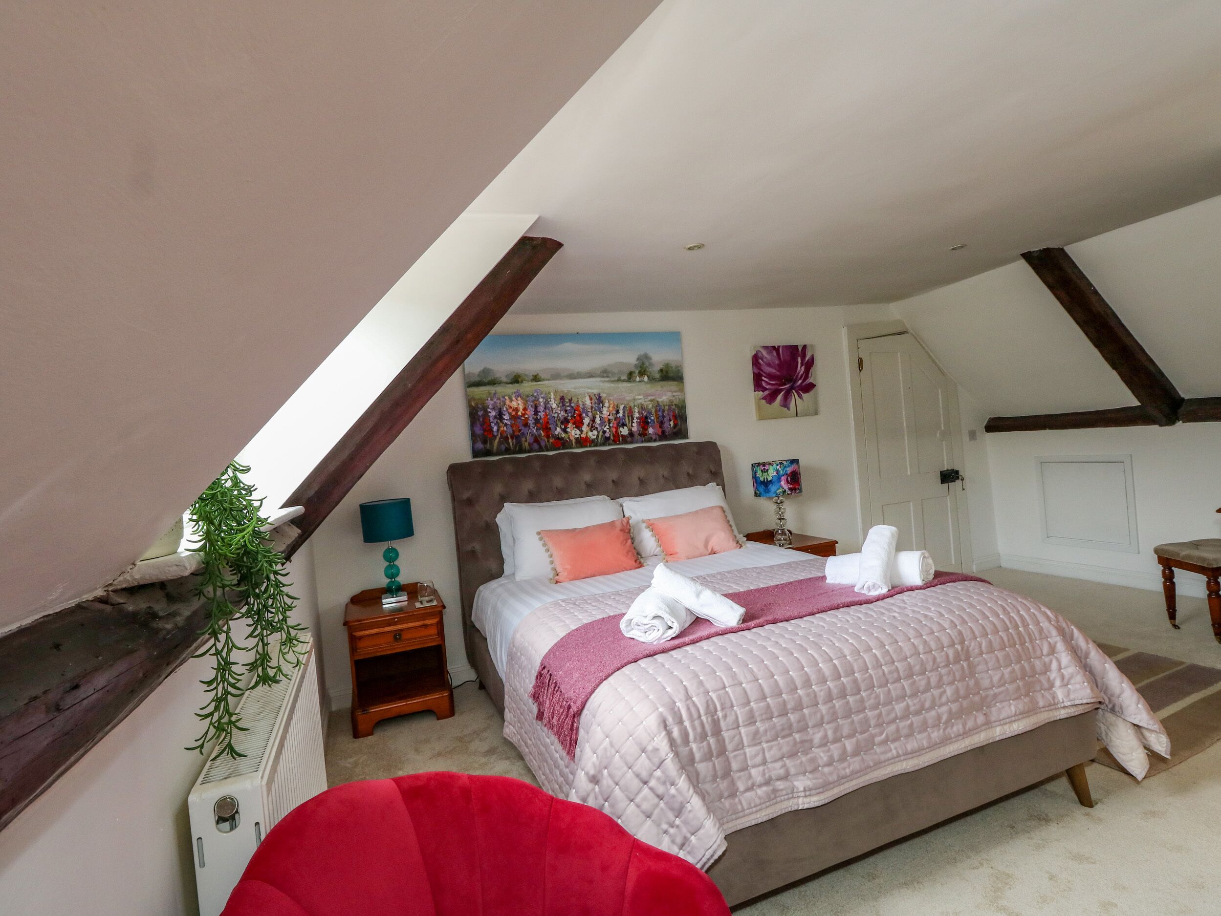 A bedroom with a large bed, a nightstand, a red chair, and a painting on the wall.