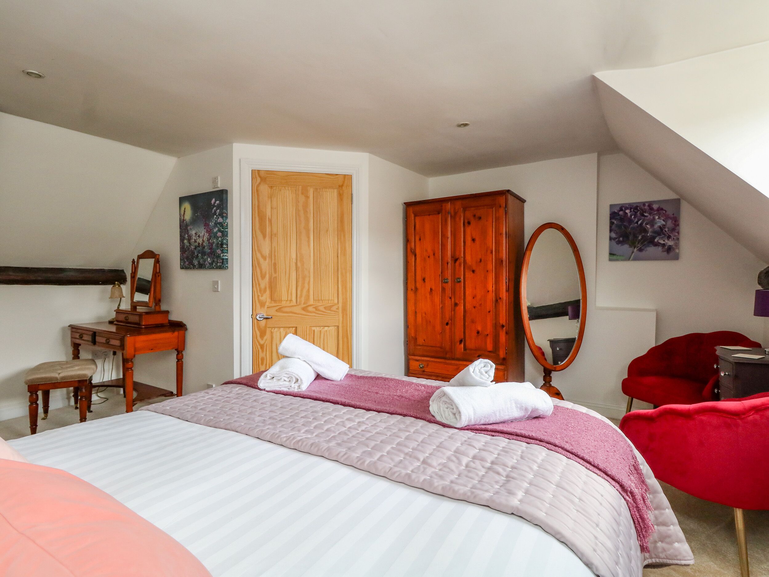 Un dormitorio con una cama, un armario de madera, una tocador con espejo y una silla roja.
