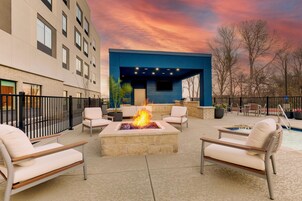 Un espacio lounge moderno al aire libre con una chimenea, asientos y una piscina.
