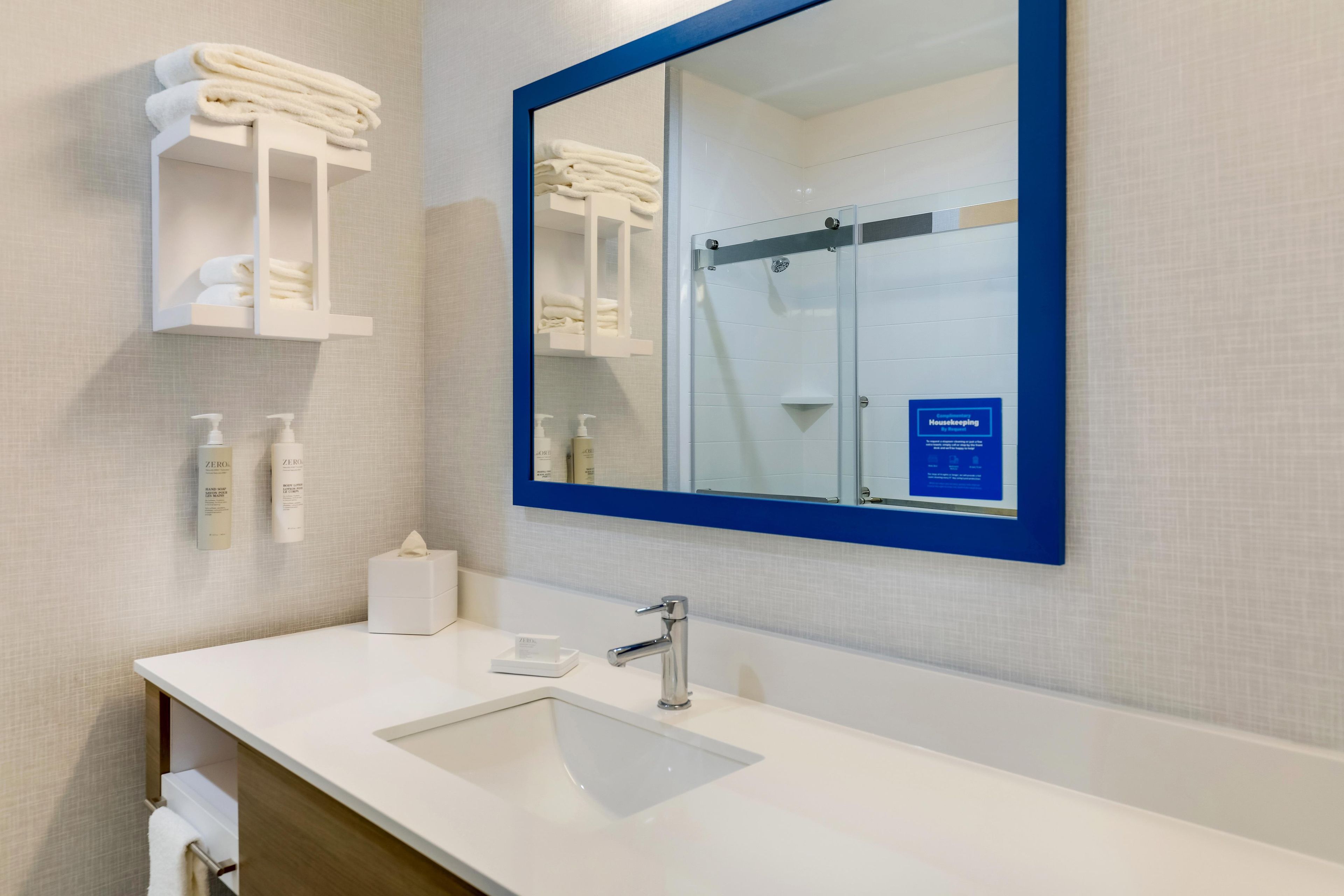 Une salle de bain moderne avec un lavabo blanc, un miroir doté d’un cadre bleu et des porte-serviettes placés au-dessus du miroir.