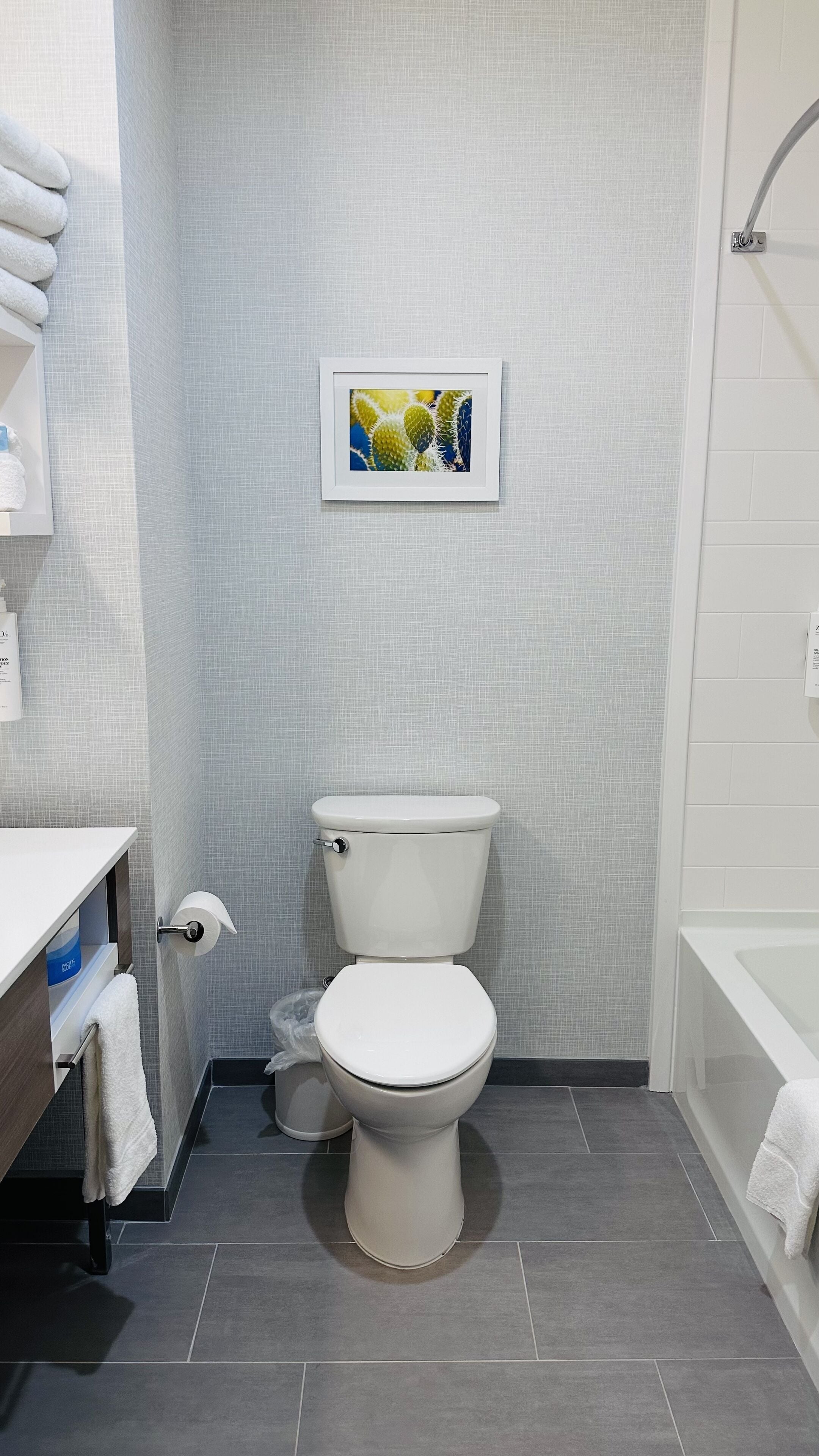 A modern bathroom with a toilet, a sink, and a bathtub. There is a framed picture on the wall above the toilet.