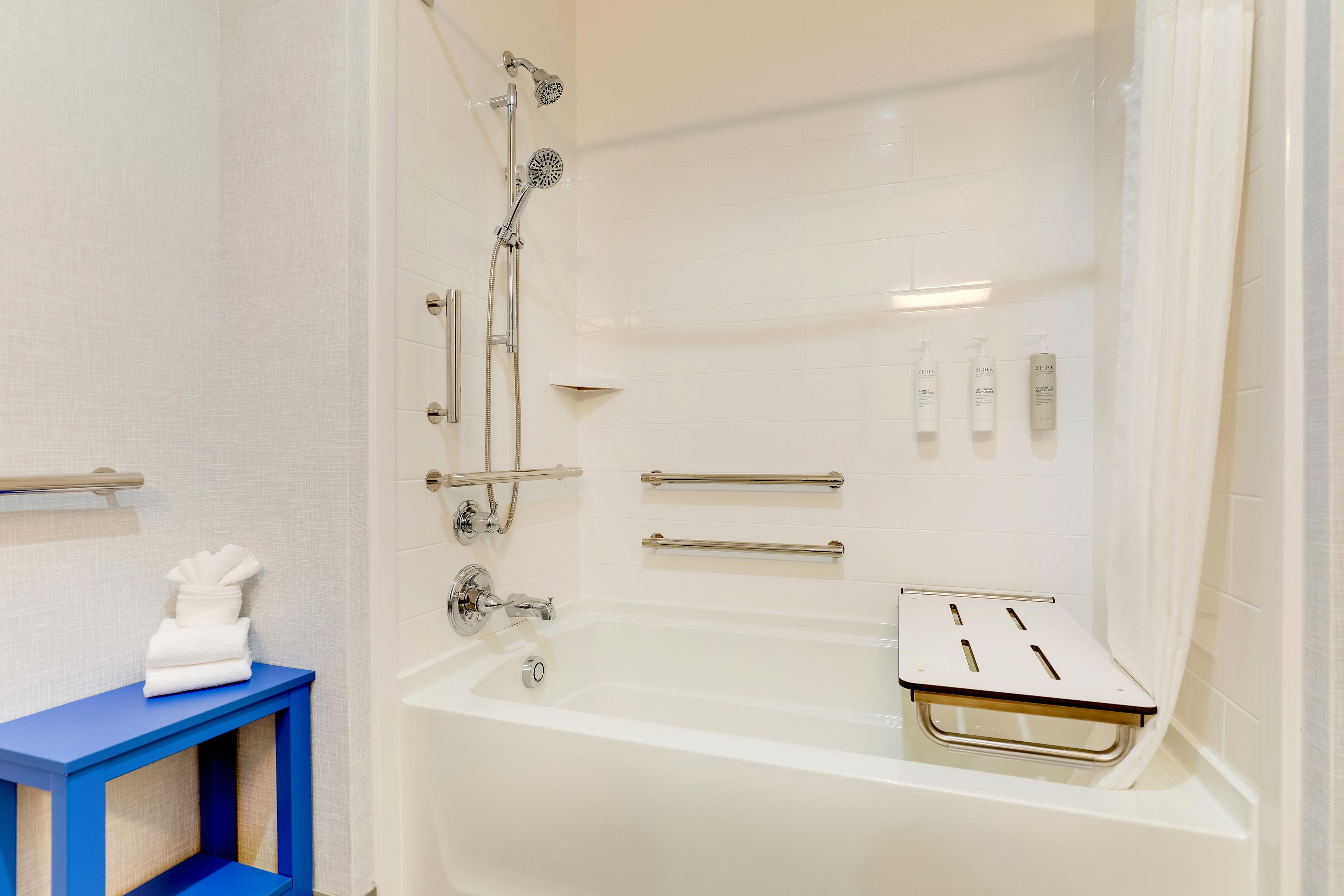A modern bathroom with a bathtub, shower, and handrails.