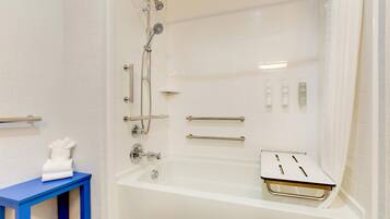 A modern bathroom with a bathtub, shower, and handrails.