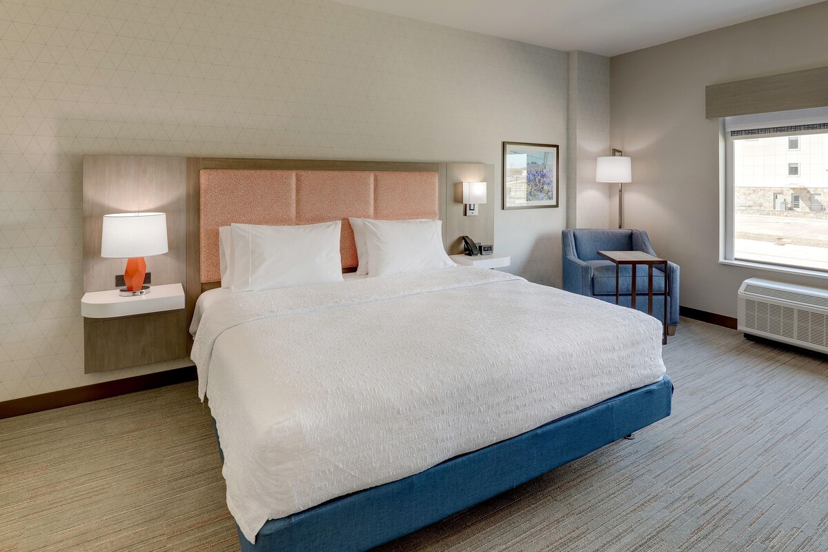 A hotel room with a large bed, bedside tables with lamps, a chair, a desk, and a window with a view.