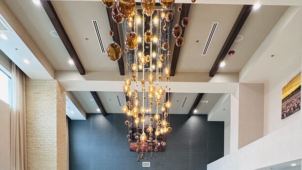 Une salle de conférence spacieuse, dotée d’une longue table, de nombreuses chaises, d’un lustre moderne et d’un grand écran mural.