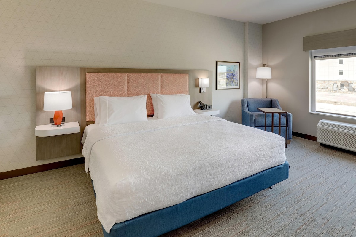 A hotel room with a large bed, bedside tables with lamps, a chair, a desk, and a window with a view.