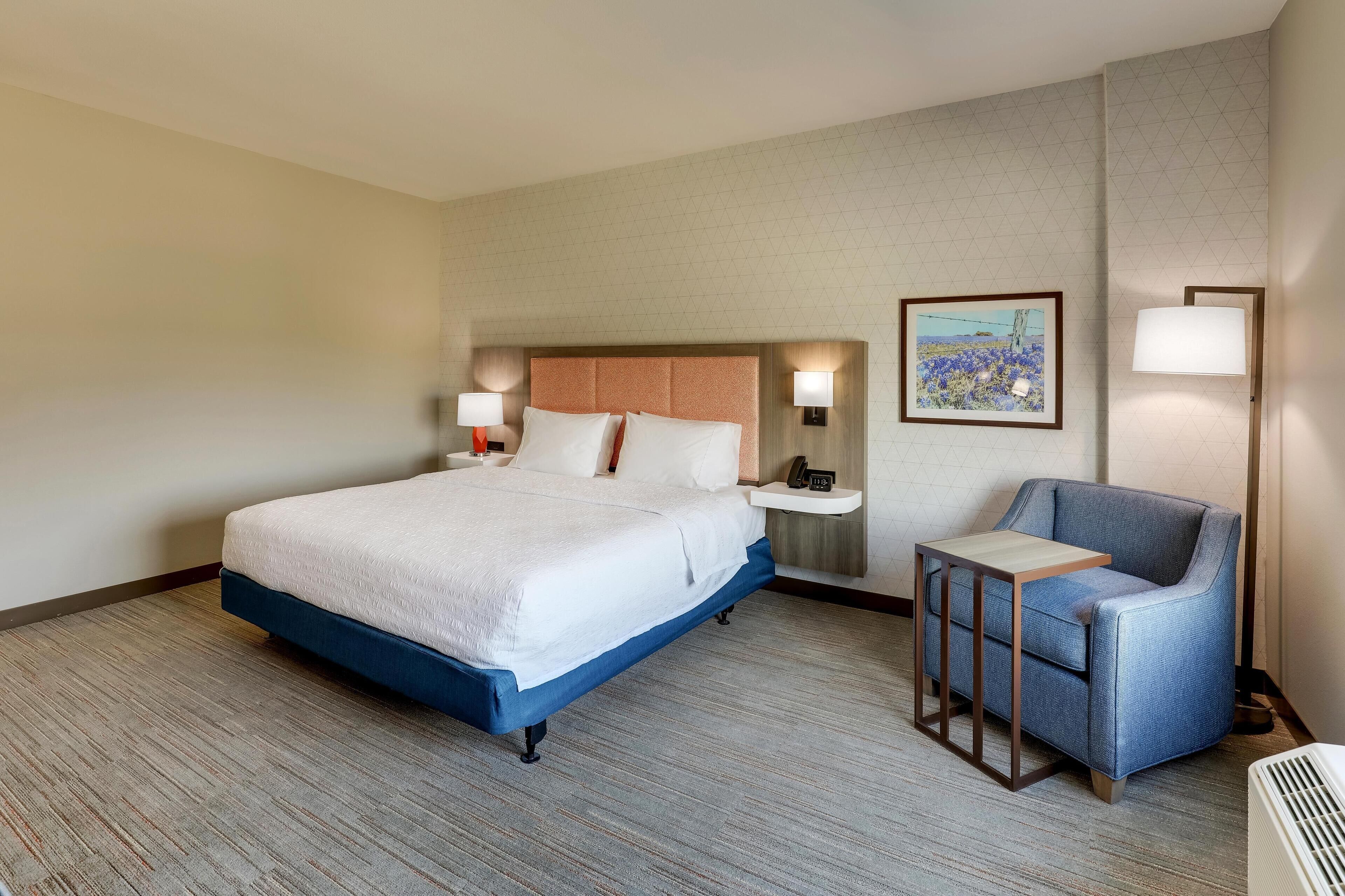 Une chambre d’hôtel avec un grand lit, des tables de chevet, une chaise et un tableau au mur.