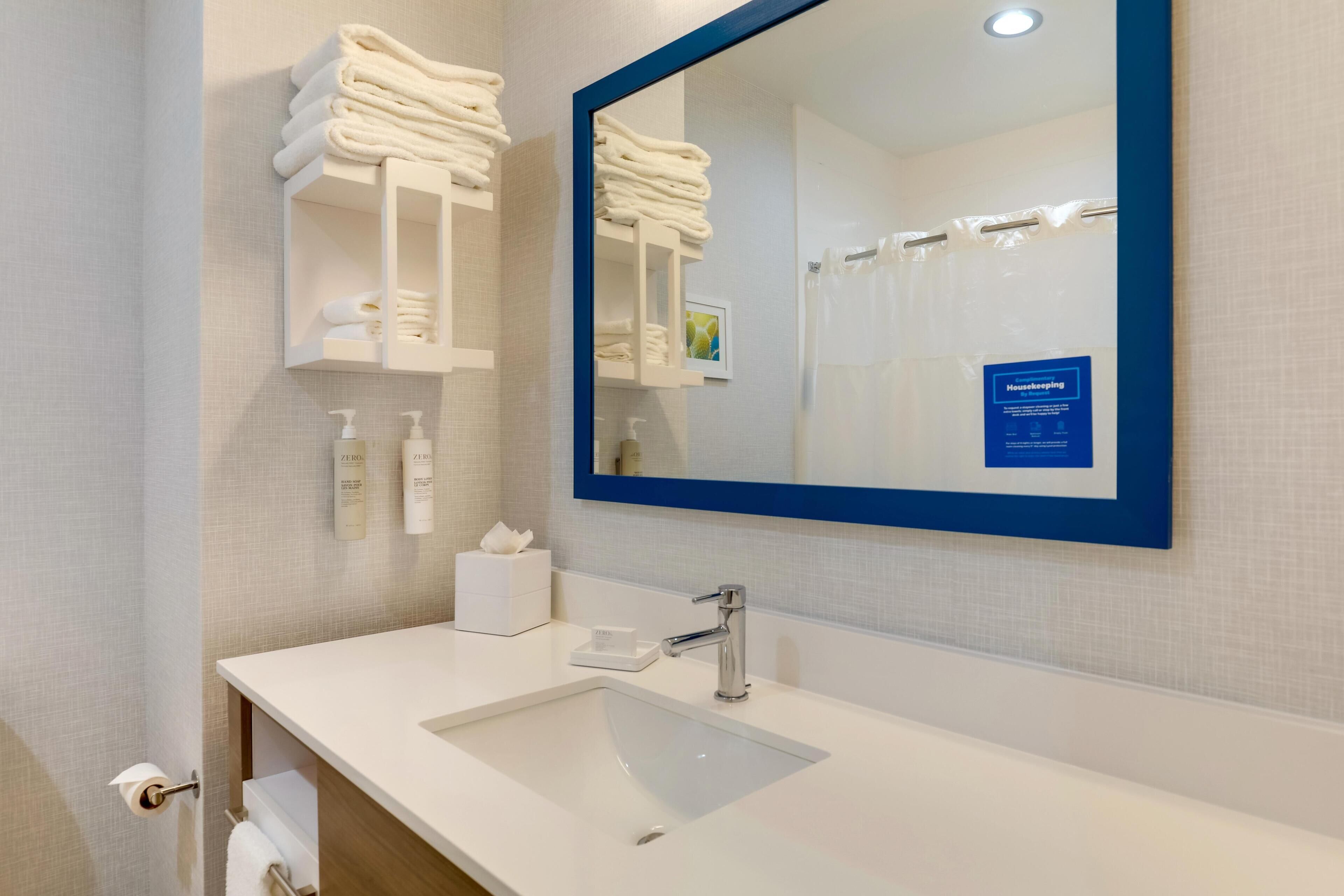 A modern bathroom with a white sink, a large mirror, and neatly stacked towels.