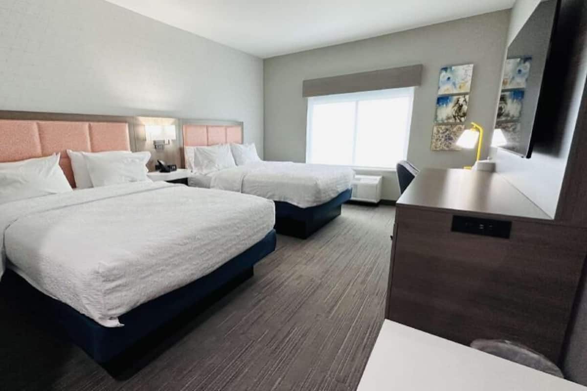 A hotel room with two beds, a desk, and a large window.