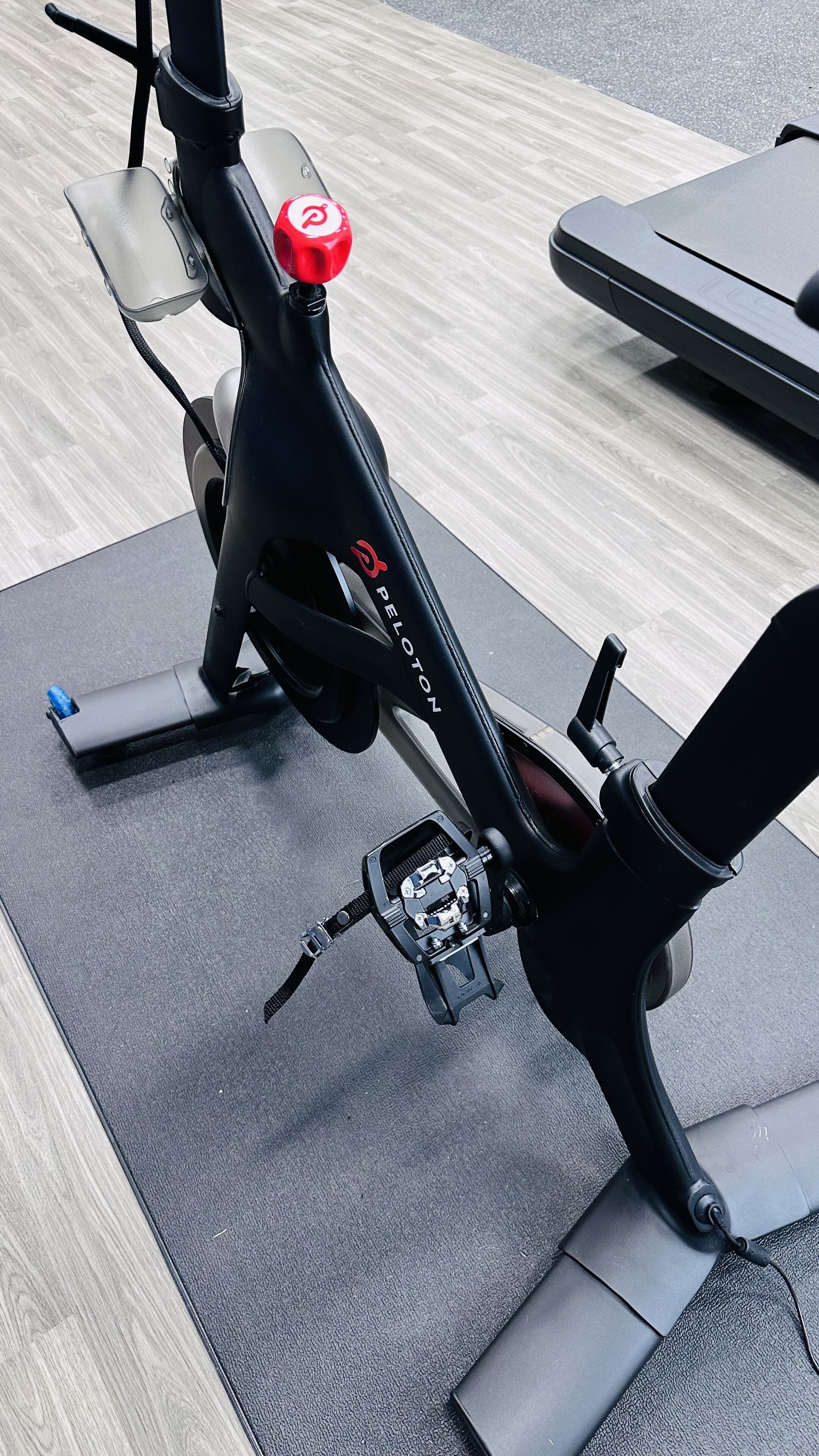 A stationary exercise bike with a red handlebar, a black frame, and the brand name "PELOTON" visible on the side.
