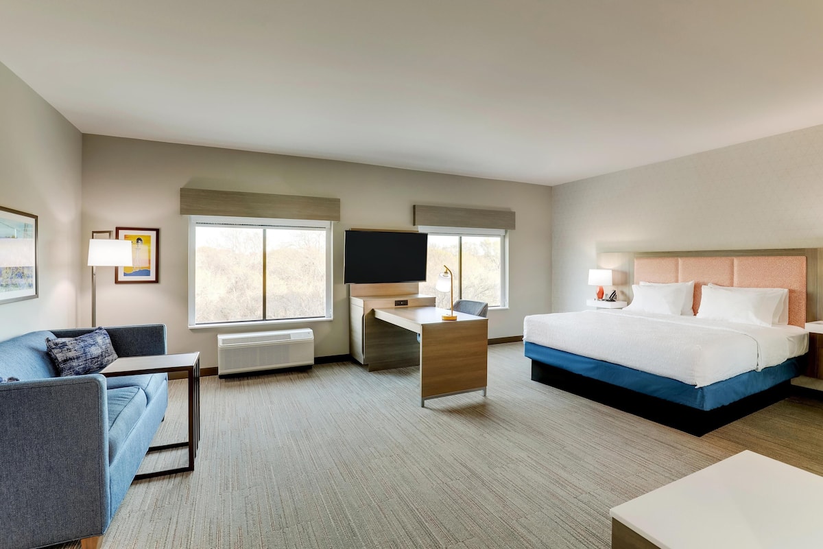 A hotel room with a bed, a desk, a chair, a sofa, and a TV.