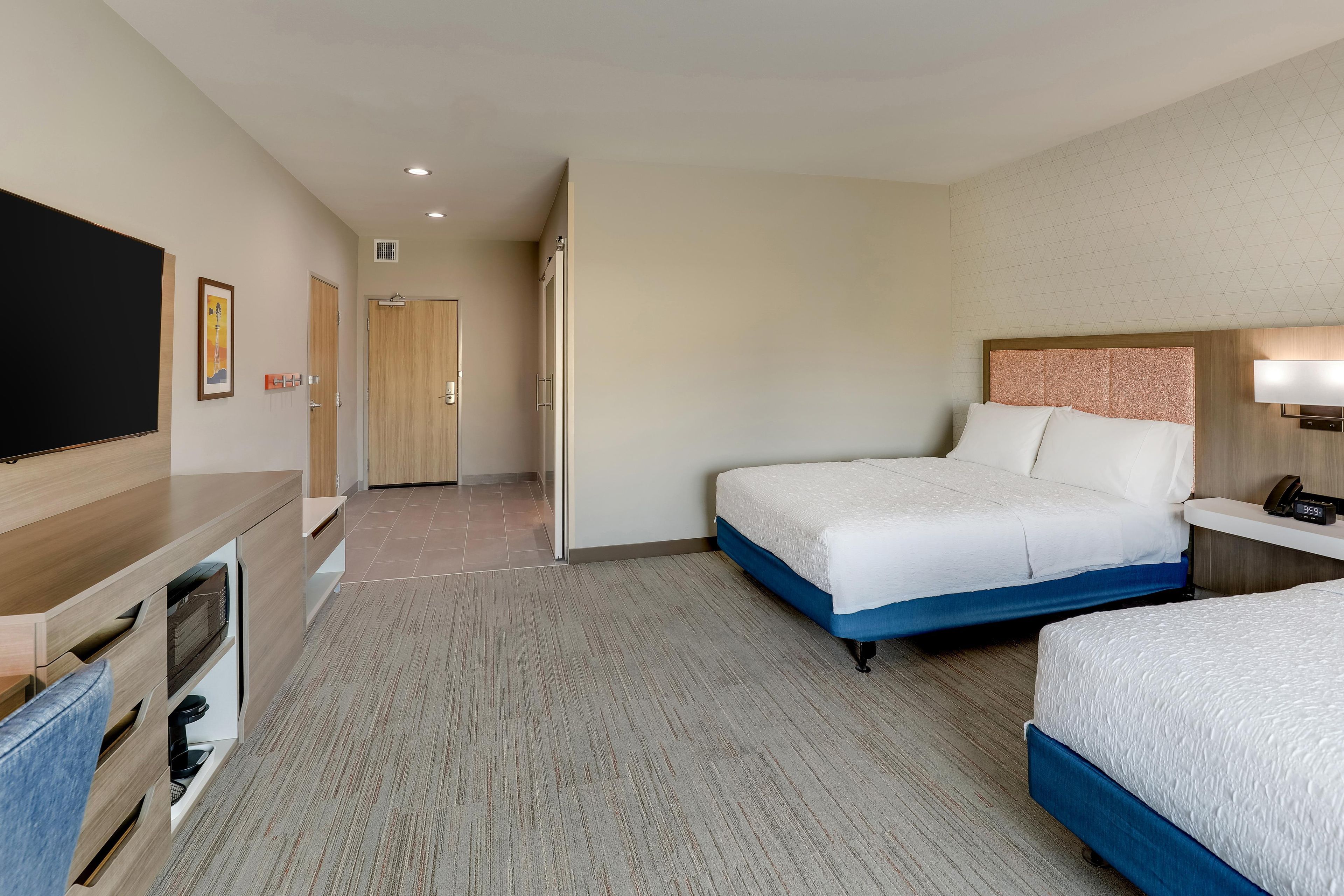 A hotel room with a bed, bedside table, TV, and a desk with a chair.