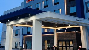 Un hôtel Hampton Inn & Suites doté d’une façade moderne, d’une entrée abritée et offrant une vue sur un ciel dégagé.