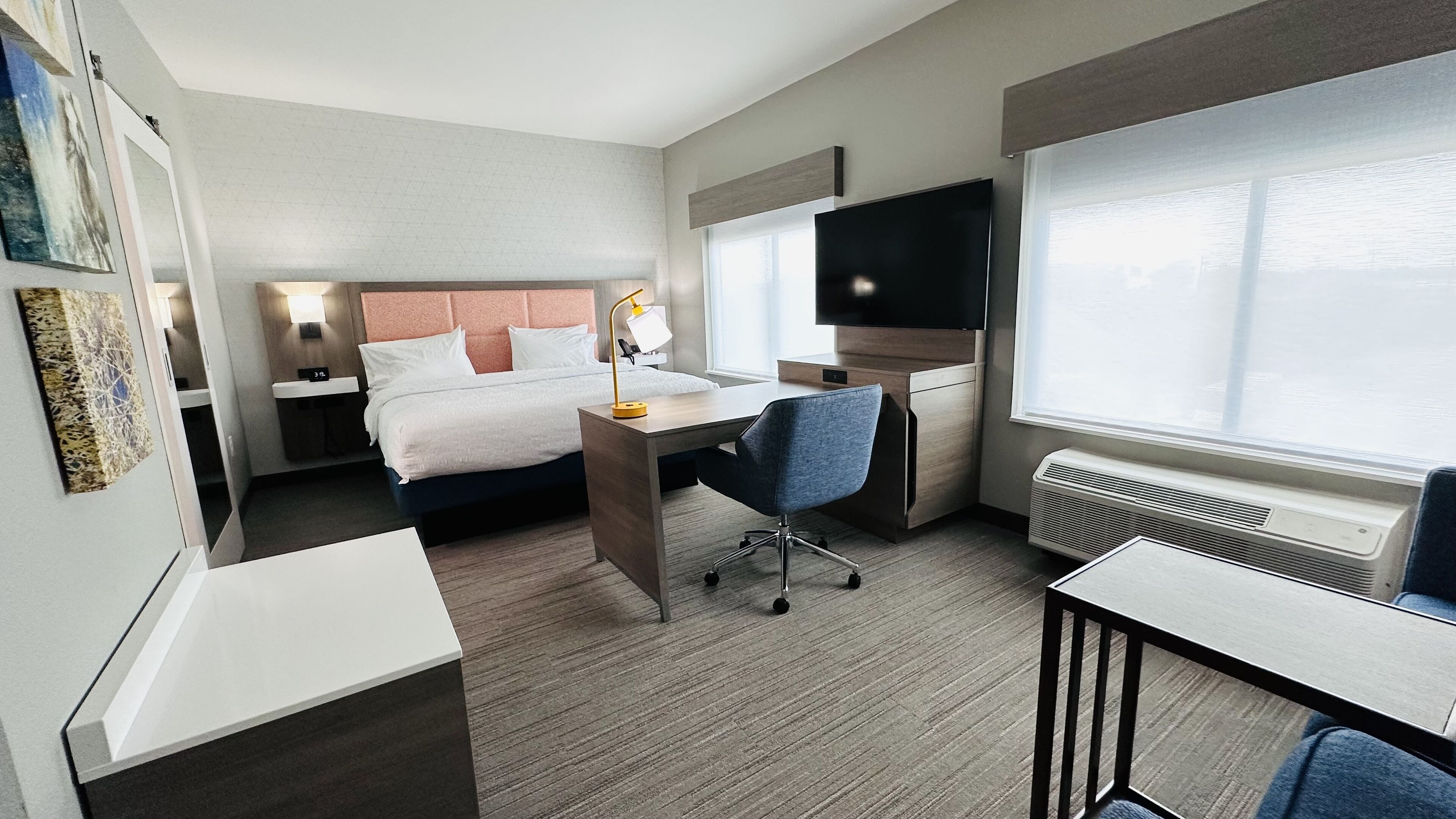 A hotel room with a bed, desk, chair, TV, and a window.