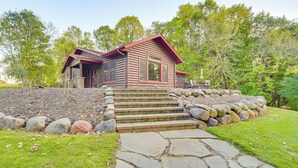 A log cabin with a stone staircase leading up to a wooden deck. - Patio, Views & Hot Tub: Quiet Lakeside Cabin (Grantsburg)