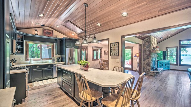 A spacious kitchen with dark cabinets, a large island, wooden chairs, and a stone accent wall. - Patio, Views & Hot Tub: Quiet Lakeside Cabin (Grantsburg)