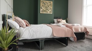A modern bedroom with two beds, a decorative leaf wall art, and a large window providing natural light. - The Callie by Sasco Apartments (Blackpool)