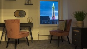 A room with a desk, two chairs, a radiator, a window with a view of a tower, and a plant on a cabinet. - The Callie by Sasco Apartments (Blackpool)