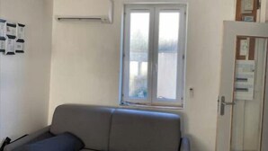 A room with a sofa, a window, and a door with a bulletin board.