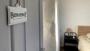 A room with a bed, a bedside table with a lamp, and a 'Bienvenue' sign on the wall.