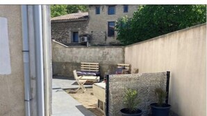 A small outdoor area with a concrete floor, a wooden bench, a potted plant, and a wall with a textured pattern.
