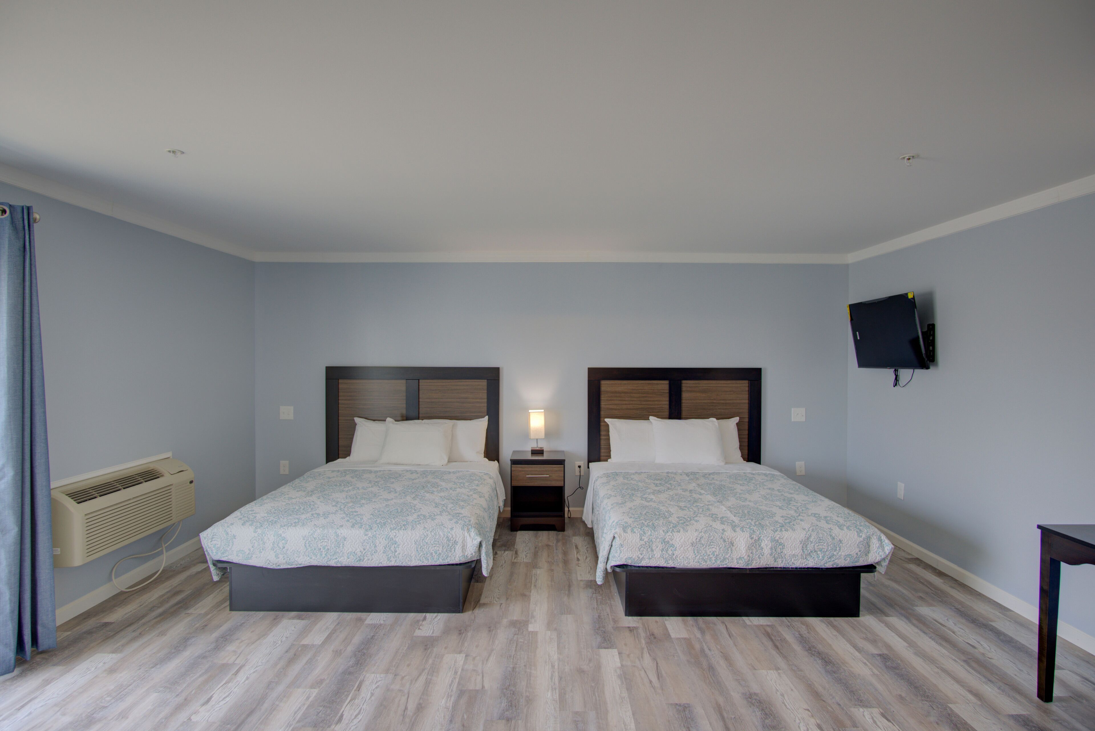Een kamer met twee bedden, een nachtkastje, een tv aan de muur en een airconditioning.