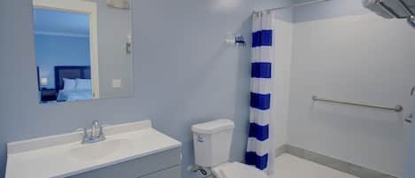 Un baño con un lavamanos blanco, un inodoro, una ducha con cortina azul y blanca a rayas, y un pasamanos.