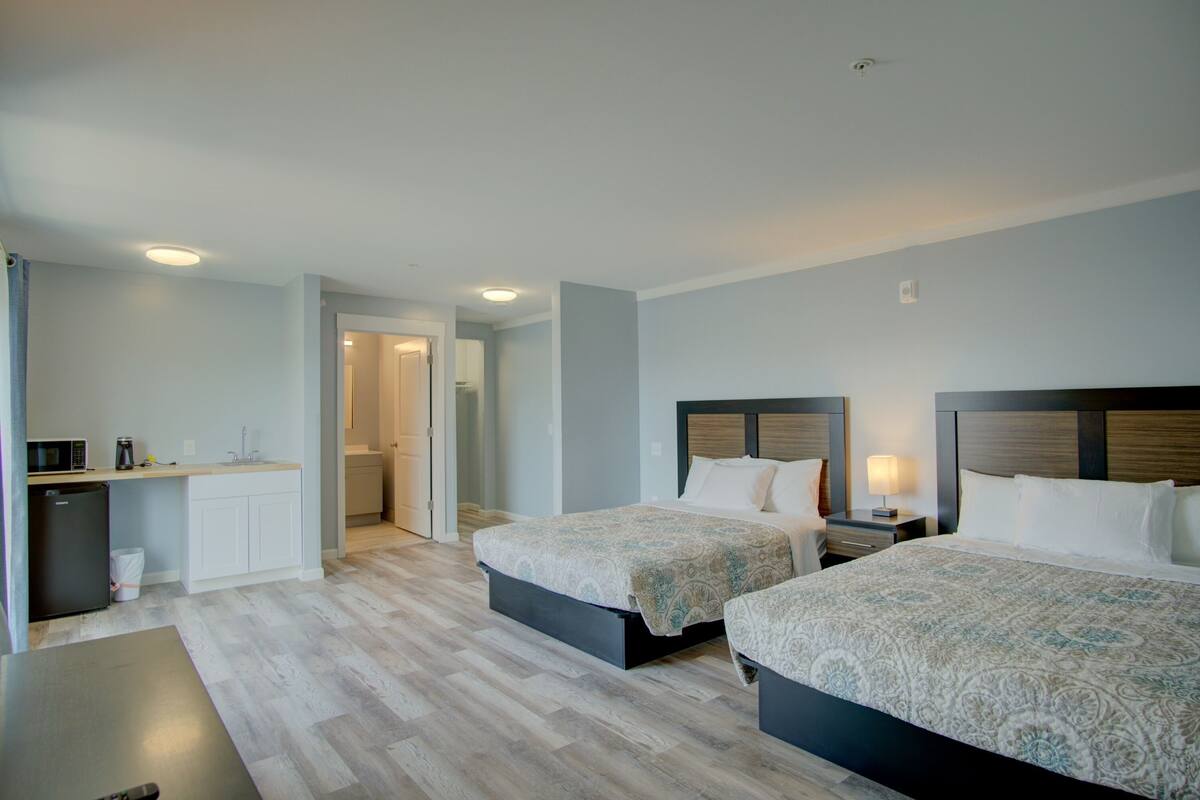 A hotel room with two beds, a small kitchenette, and a bathroom visible through an open door.