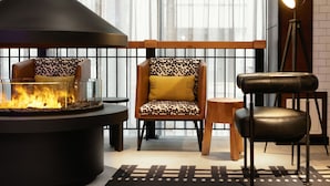 Un salón moderno con una chimenea central, dos sillones estampados, un taburete de cuero y una lámpara de pie.