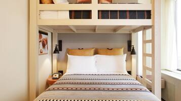 Habitación con literas, una colcha estampada, una mesita de noche con lámpara y una ventana con cortinas.