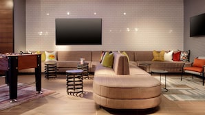 Una sala de estar moderna con un sofá seccional, una mesa de futbolín y un televisor de pantalla plana montado en la pared.
