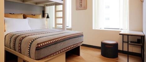 A bedroom with a bed, a desk, a chair, a window, and a hanging light fixture.
