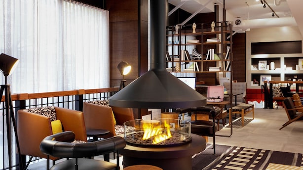 Un área de estar moderna con asientos de cuero, una chimenea central y una estantería al fondo.
